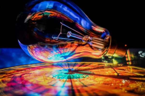 A clear incandescent light bulb lies on its side, reflecting and refracting vibrant, colorful lights and patterns beneath it.