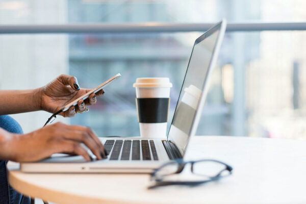 A person using a smartphone while typing on a computer