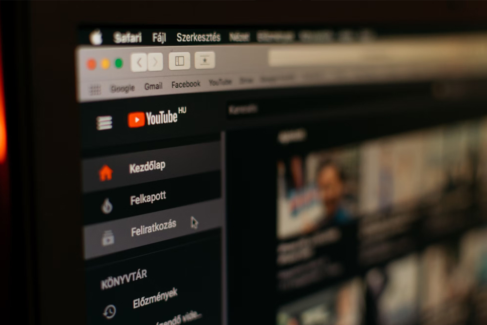 videos A computer screen displays the YouTube homepage in Hungarian, showing menu options and a blurred video feed in dark mode.