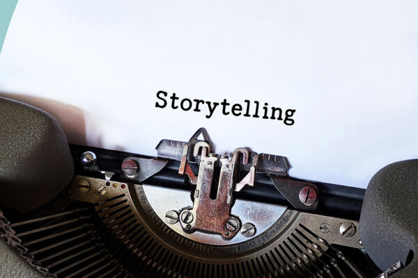 A close-up of a typewriter with a sheet of paper displaying the word "Storytelling" typed in black letters.